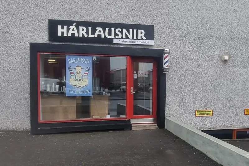 Stofan að utan: rauð hurð og rakarastöng undir skiltinu Hárlausnir